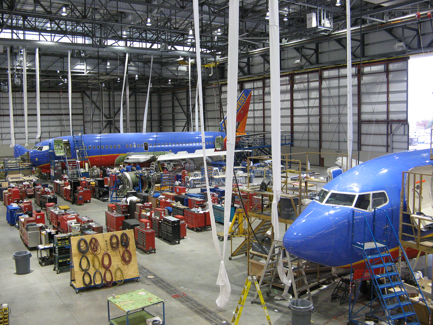 Two commercial aircraft undergo maintenance inside a large steel-framed aviation hangar, demonstrating the expansive space and structural performance required for complex aviation operations.