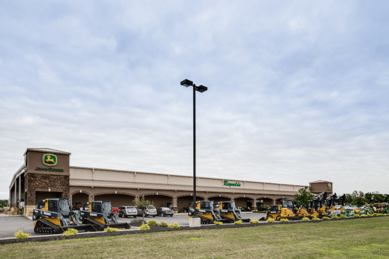 John Deere equipment dealership exterior with skid steers and machinery displayed in front of a large retail building.