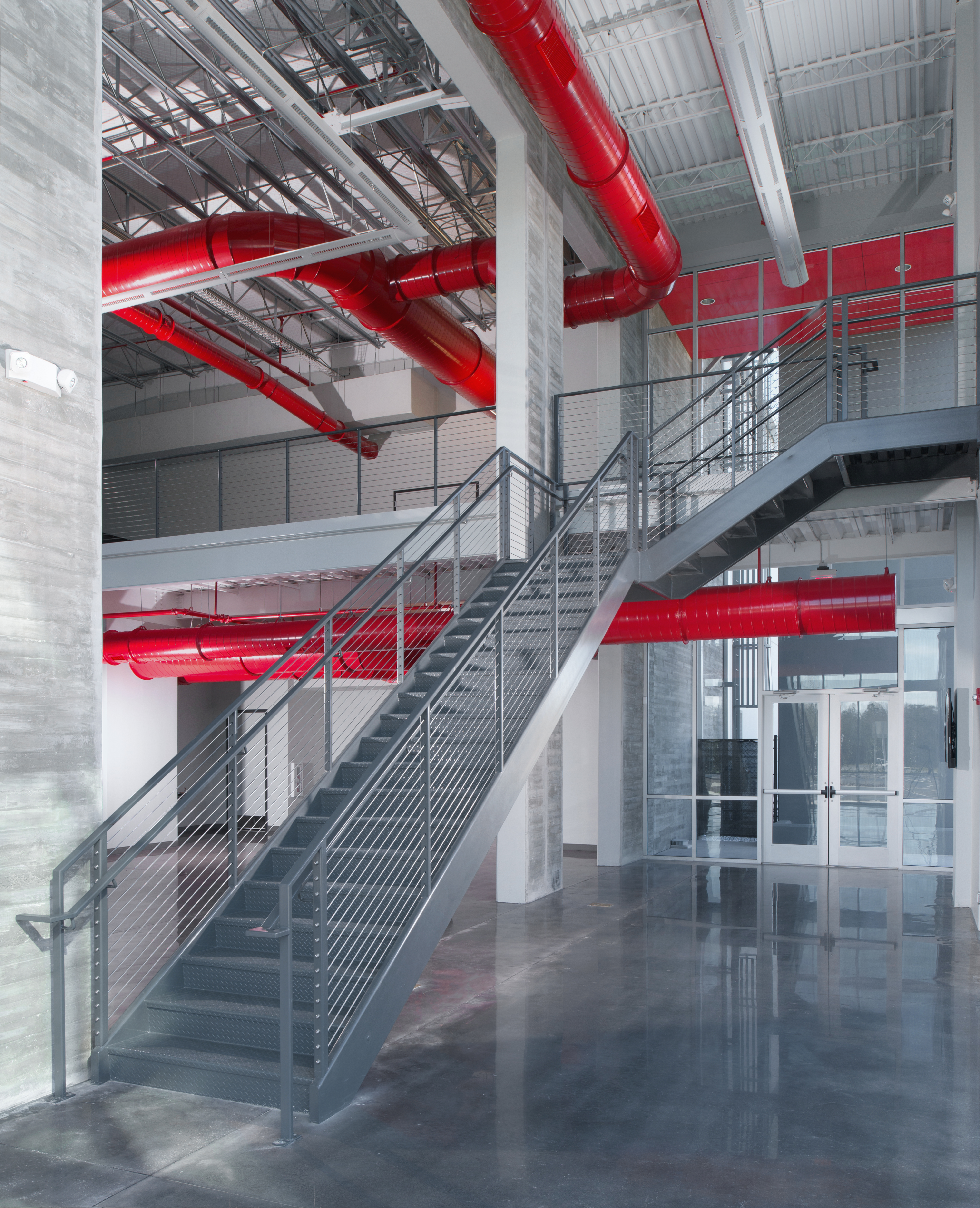 Modern commercial building interior with exposed red ductwork, steel staircase, and polished concrete floors.