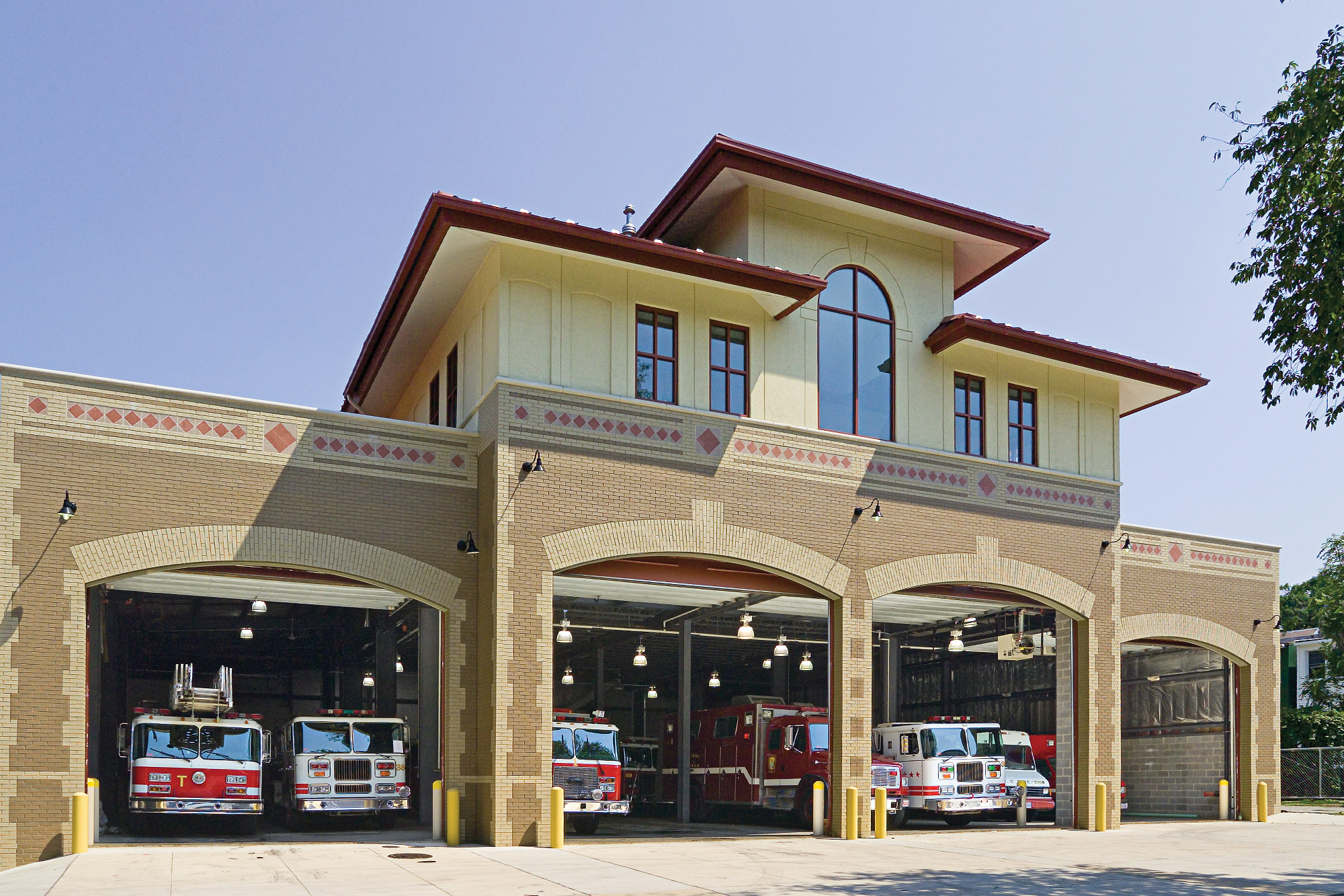 Brick fire station with open garage bays, warm yellow lighting and red emergency vehicles beneath a deep blue evening sky.
