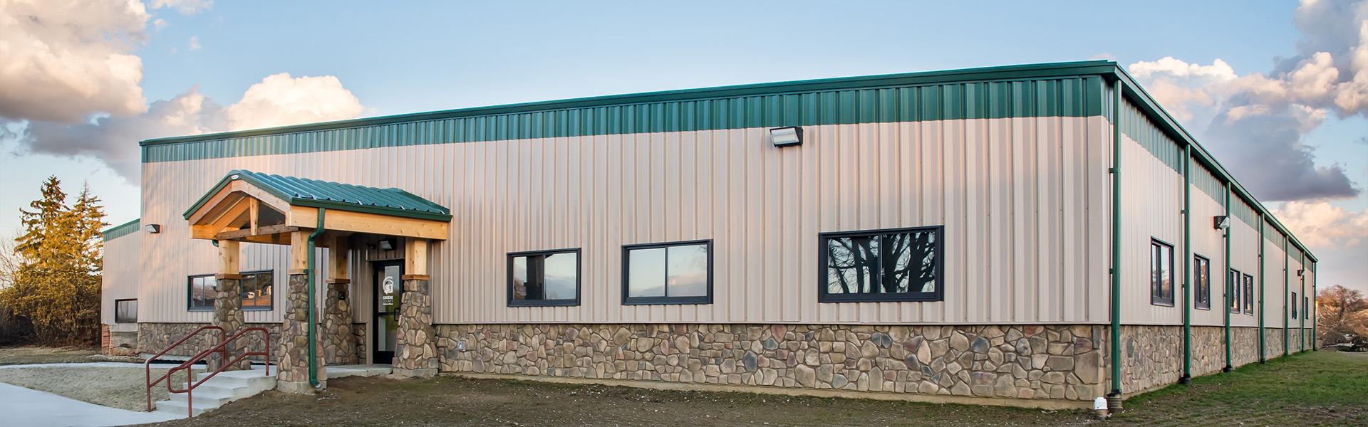 Metal parks facility with tan vertical rib siding, green roof trim, stone wainscot and a covered entry