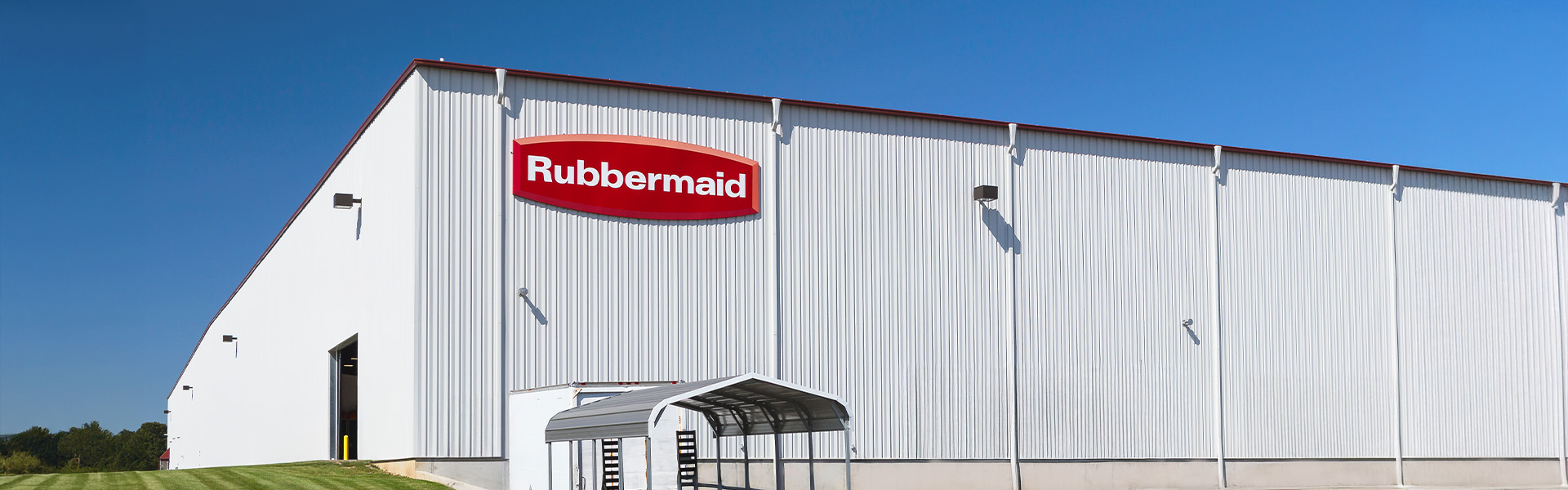 Exterior of a white Rubbermaid warehouse with a large open garage door and metal awning in the front.