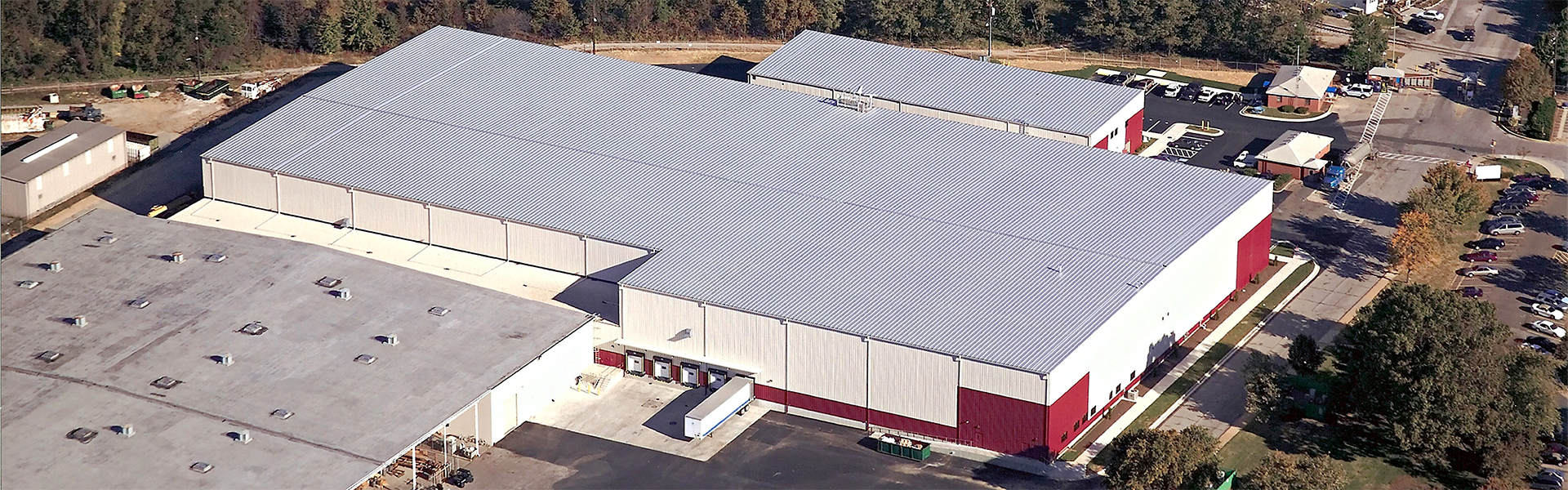 Aerial view of a large warehouse with white metal roof, red wall accents and adjacent industrial buildings