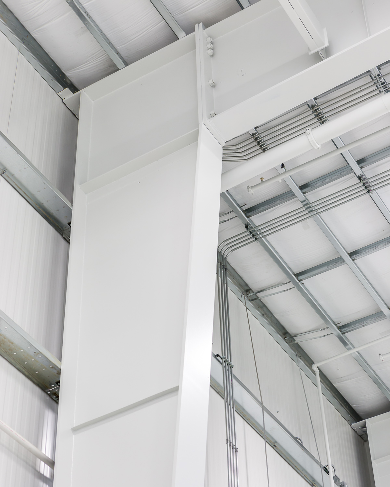 Close-up of a white steel column and beam connection with roof purlins and cable trays