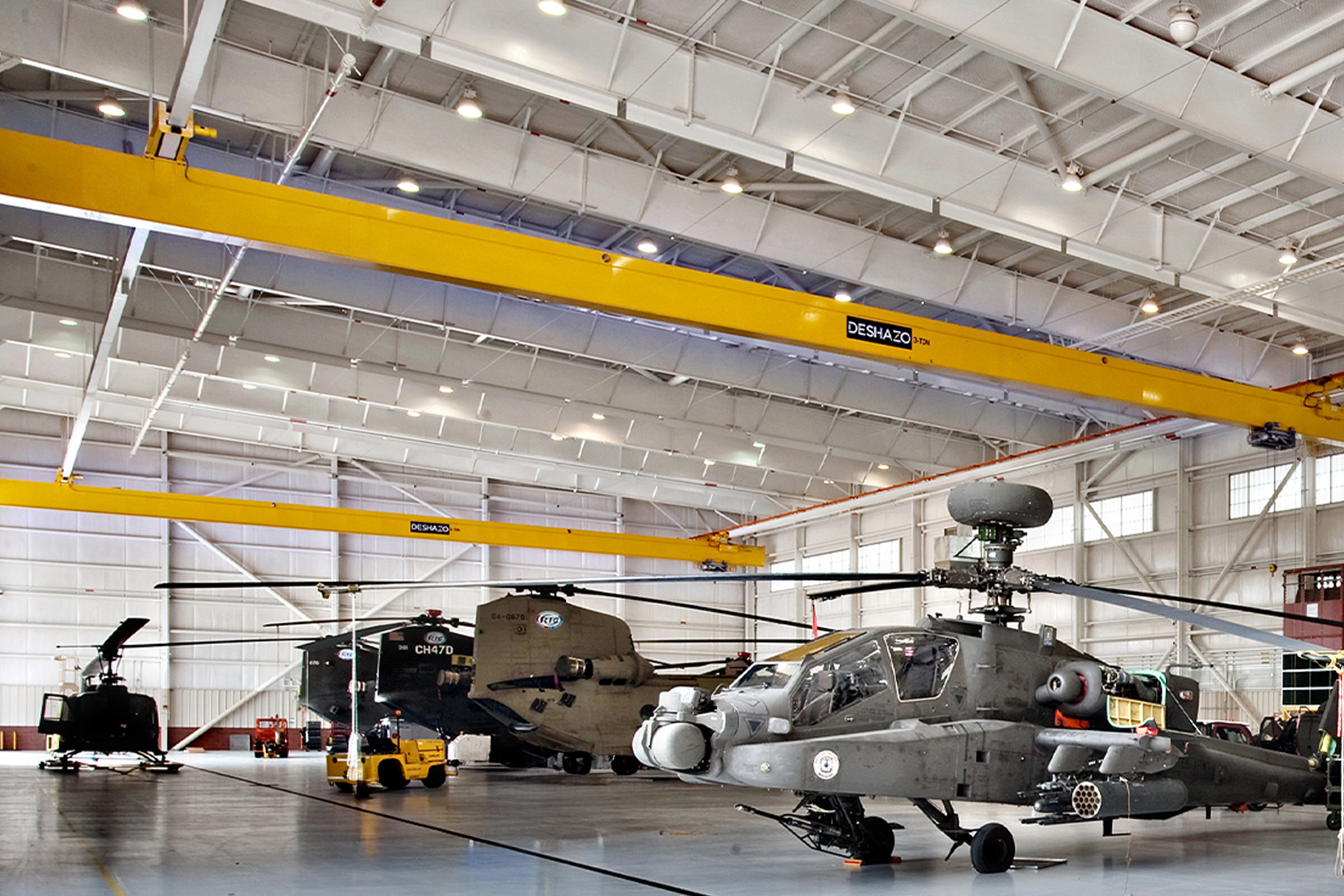 Aircraft hangar interior with white steel framing, yellow bridge cranes and military helicopters
