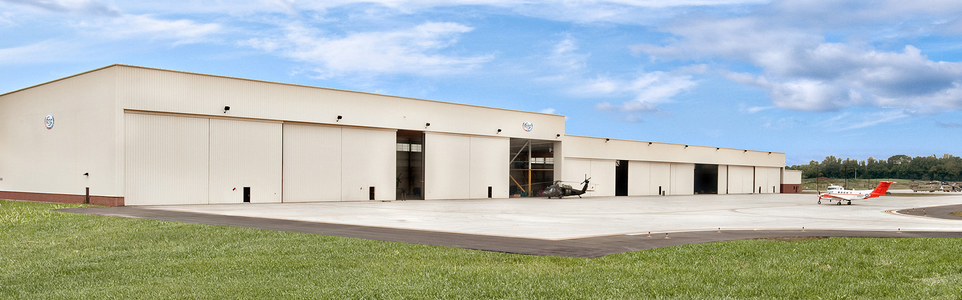 Beige aircraft hangar with vertical rib wall panels, large sliding door opening and concrete apron