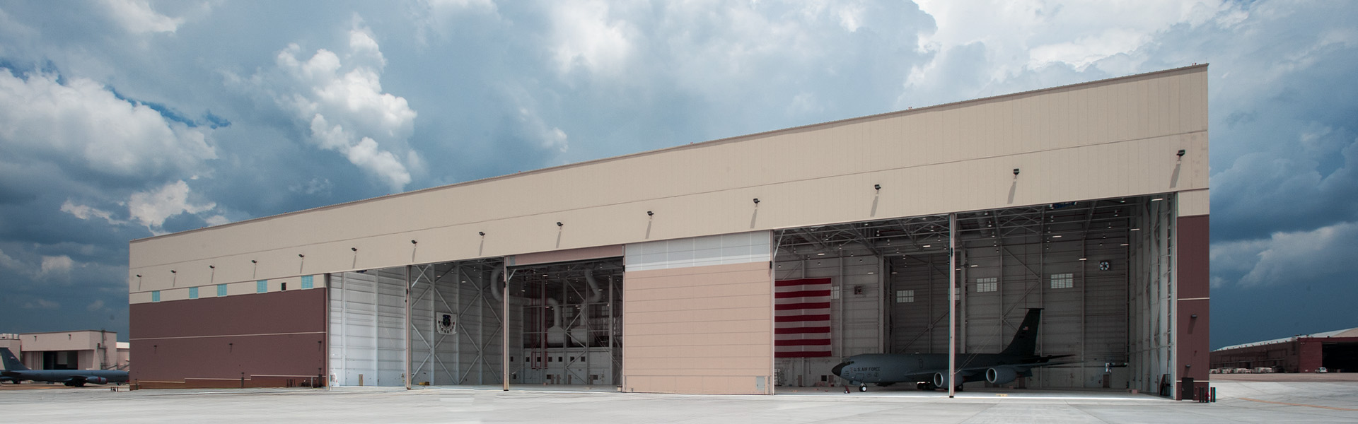 Large military aircraft hangar with beige metal wall panels and multiple open bay doors