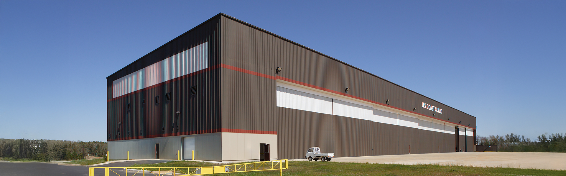 Large miliary consolidated hangar with dark brown vertical rib wall panels, red accent band and a white ribbon stripe
