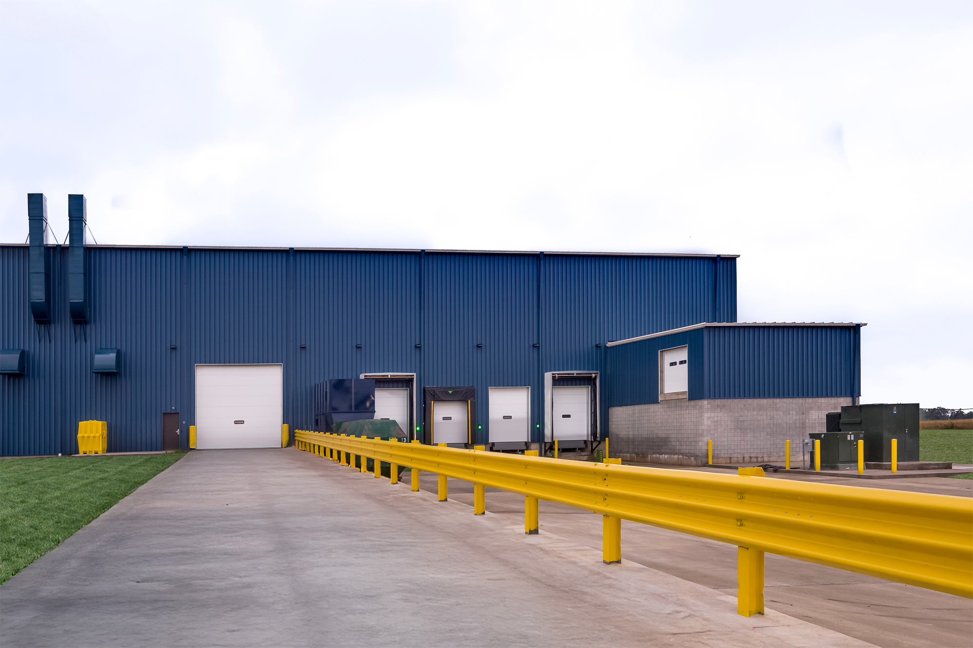 Blue metal manufacturing building with vertical rib wall panels and yellow guardrail