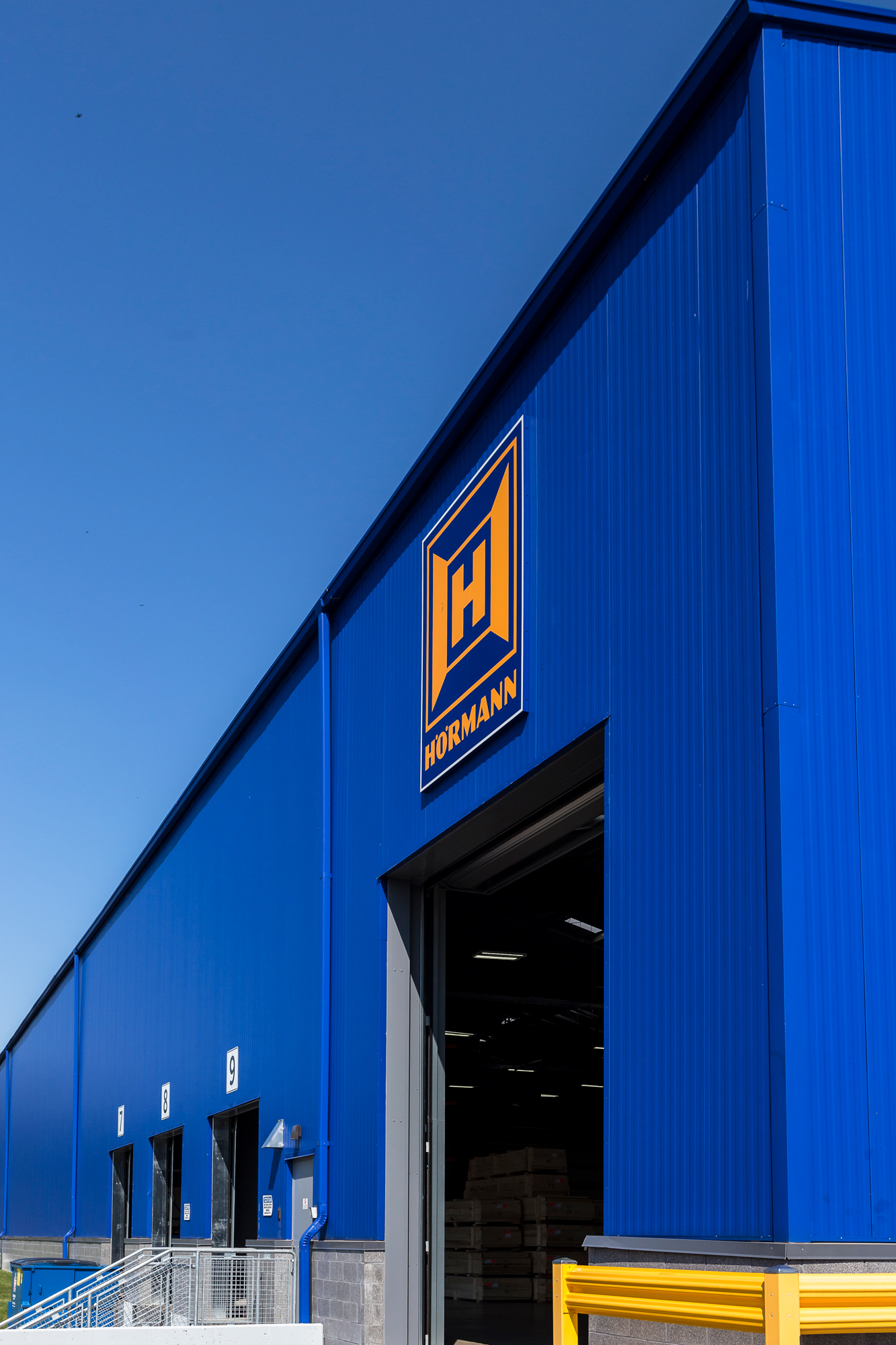 Close-up of blue vertical rib metal wall panels with a large overhead door and loading bays