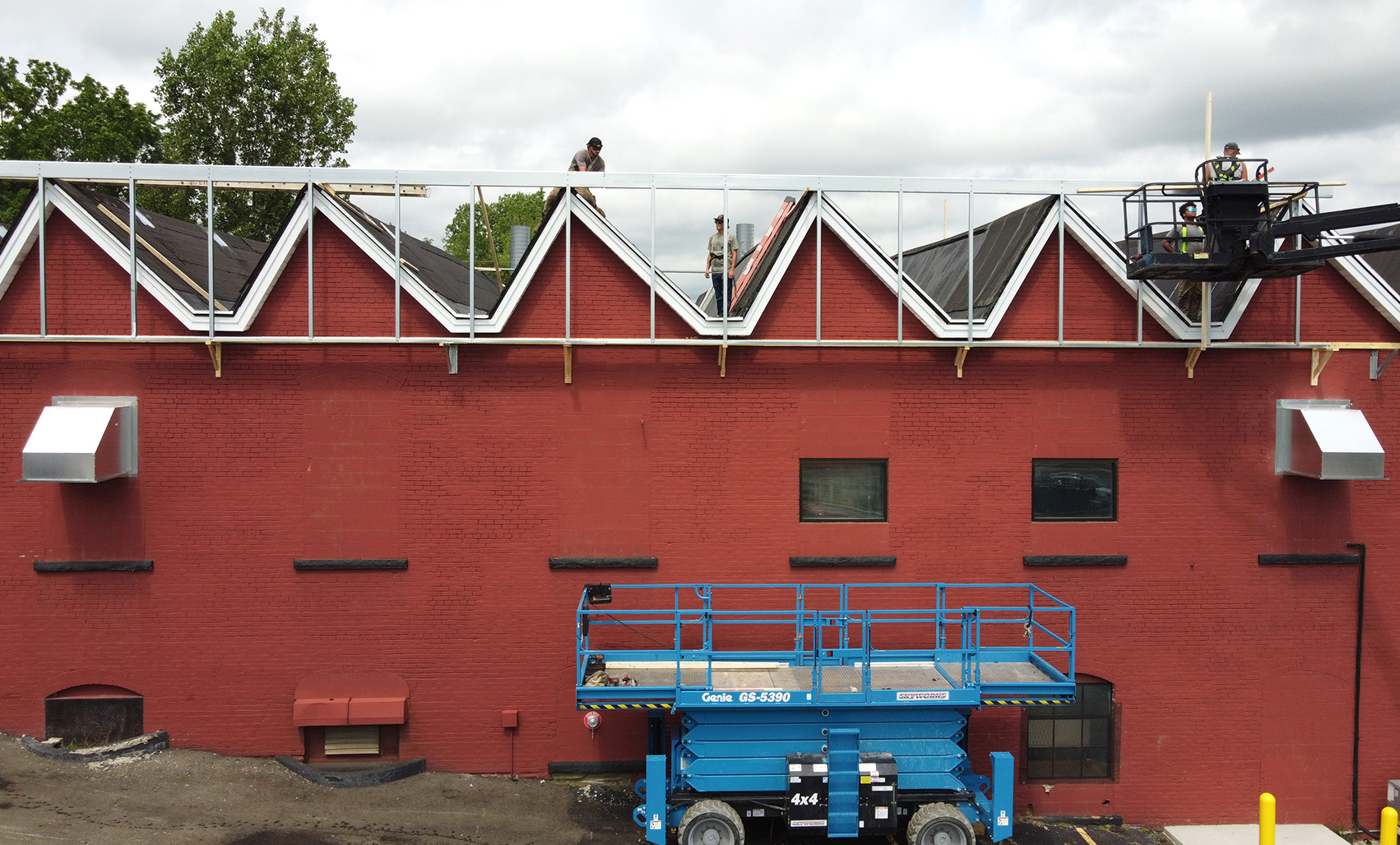 Construction crews install a new steel roof framing system above an existing red brick building, demonstrating Butler’s engineered retrofit solutions for extending building performance and service life.