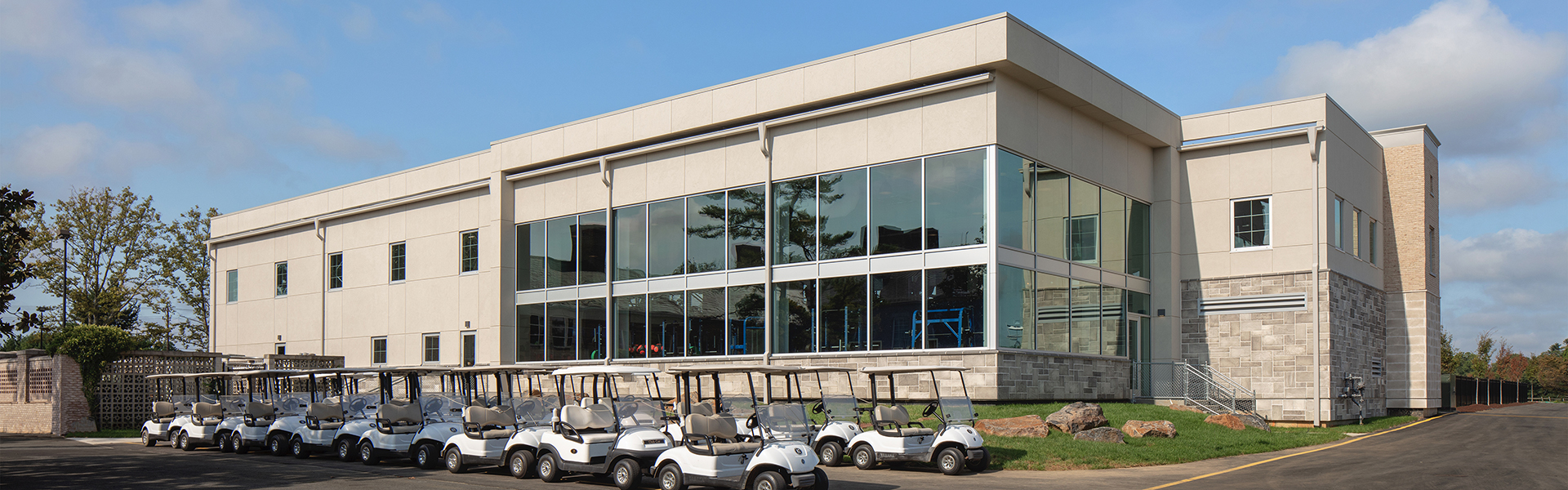 Modern country club building with large glass windows and stone exterior, with golf carts parked outside.