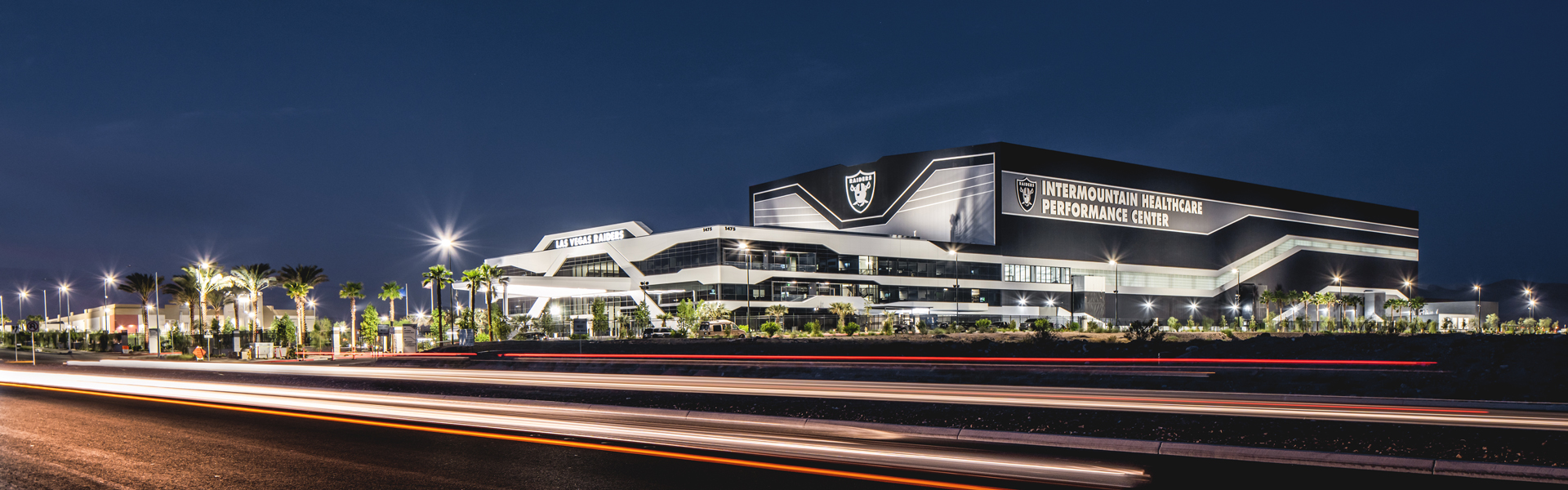 Las Vegas Raiders Practice Facility exterior at night with illuminated facade and sweeping rooflines