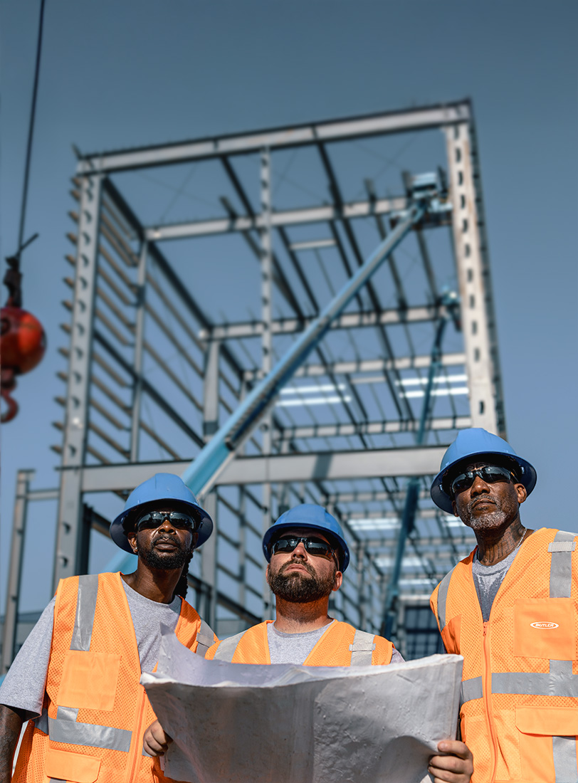 Construction workers reviewing site plans with metal framed building in background