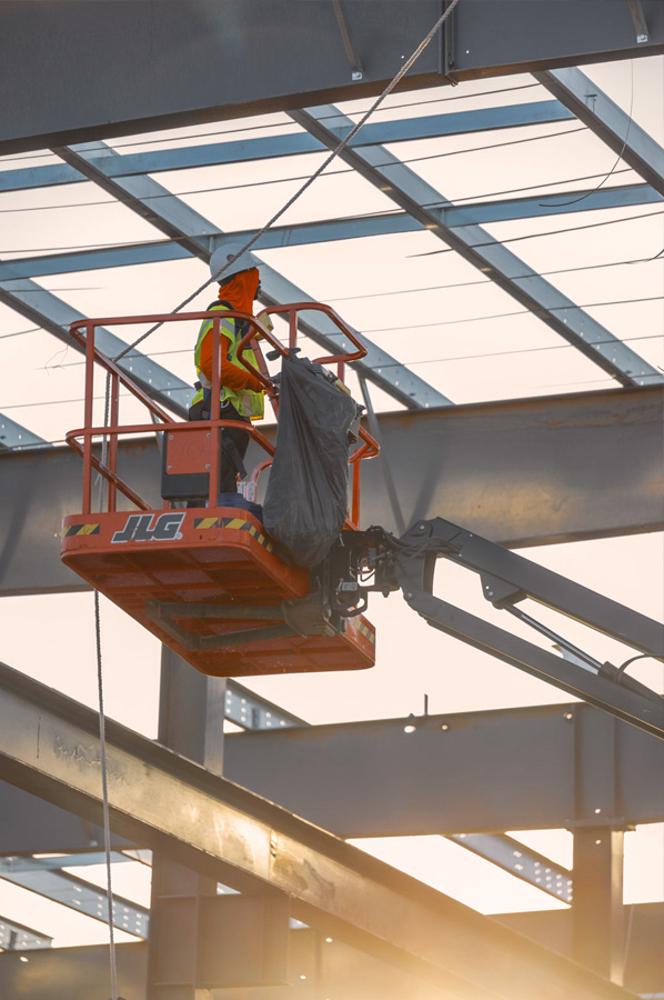 Worker installing roof structure from lift during steel building erection.