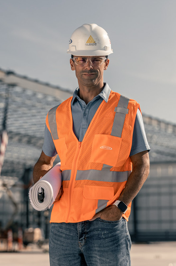 Builder with hard hat and plans standing at a job site representing industry expertise in steel construction.