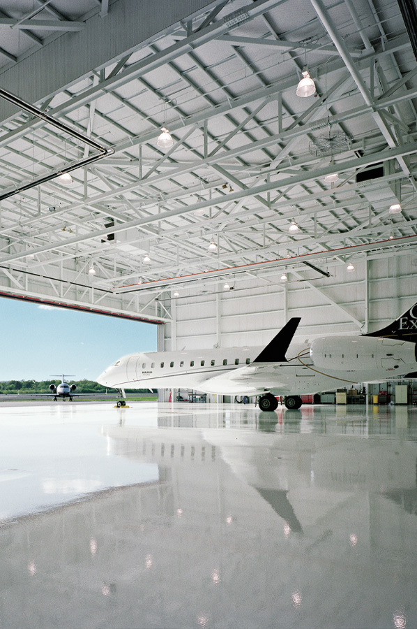 Aircraft inside a bright hangar with white steel roof framing and large open door