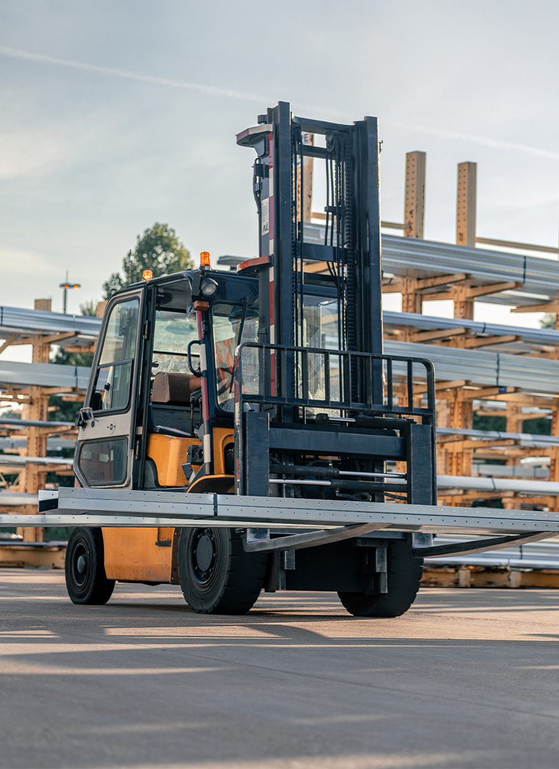 Yellow forklift transporting steel beams outdoors