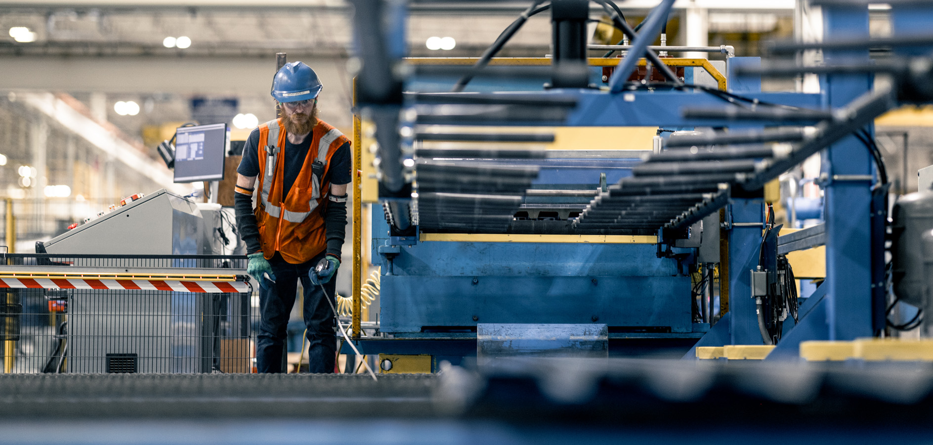 Worker in hard hat and safety vest inspecting a blue automated production line in an industrial manufacturing facility