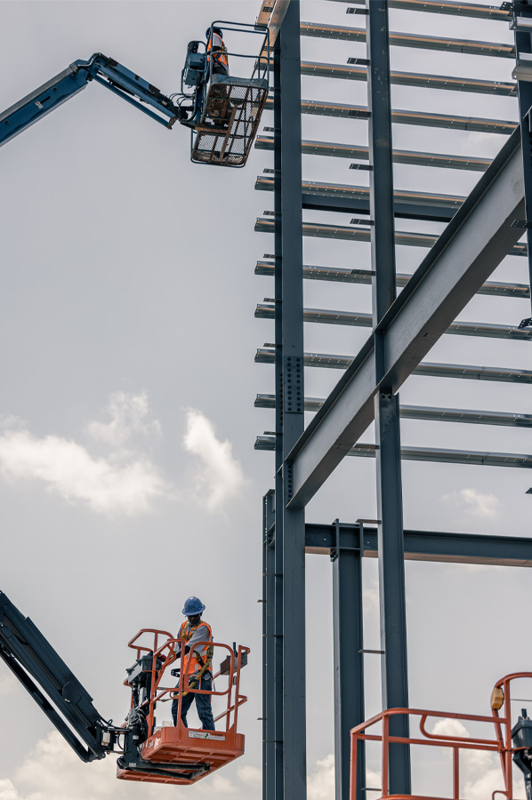 Steel building construction workers on aerial lifts at site